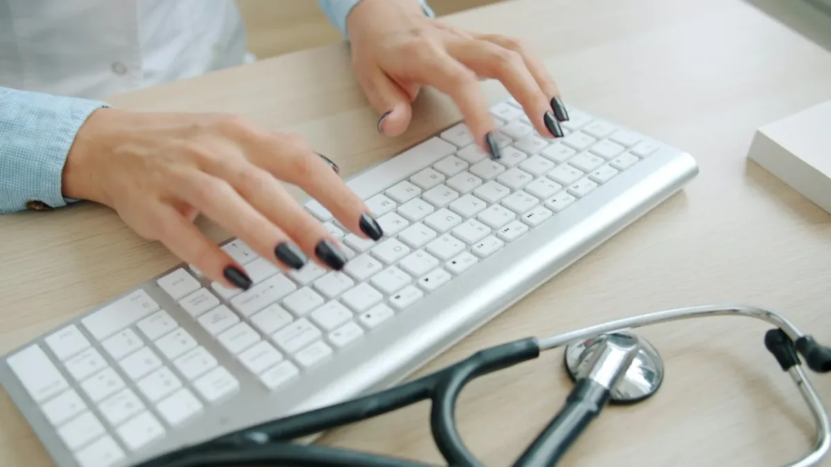 Mãos digitando em teclado ao lado de um estetoscópio
