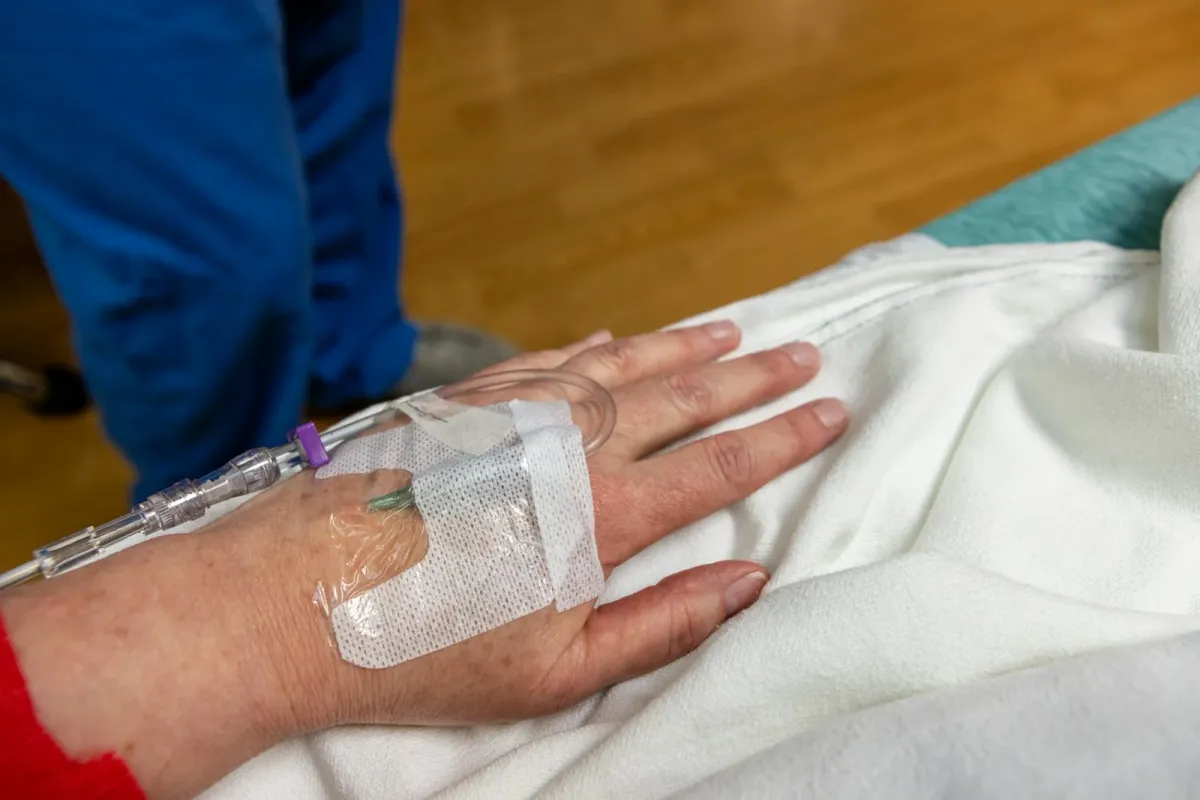 Mão de paciente com acesso venoso periférico fixado, no leito