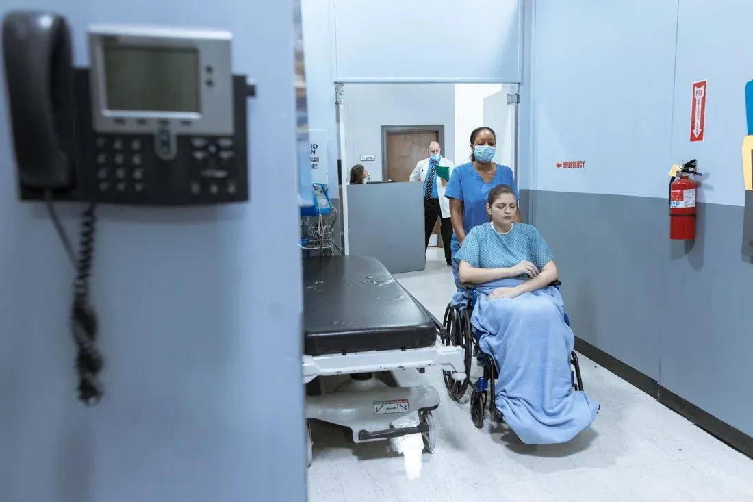Paciente em cadeira de rodas acompanhado por equipe em corredor hospitalar