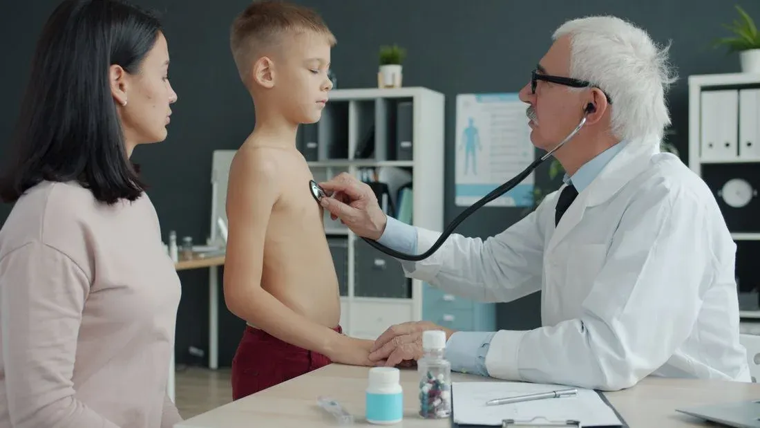 Médico ausculta o tórax de um menino em consulta, acompanhado da mãe