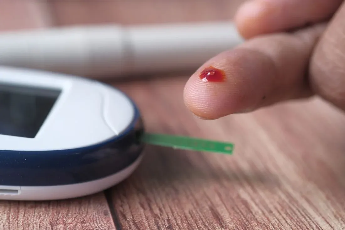 Gota de sangue na ponta do dedo ao lado do glicosímetro e da fita reagente