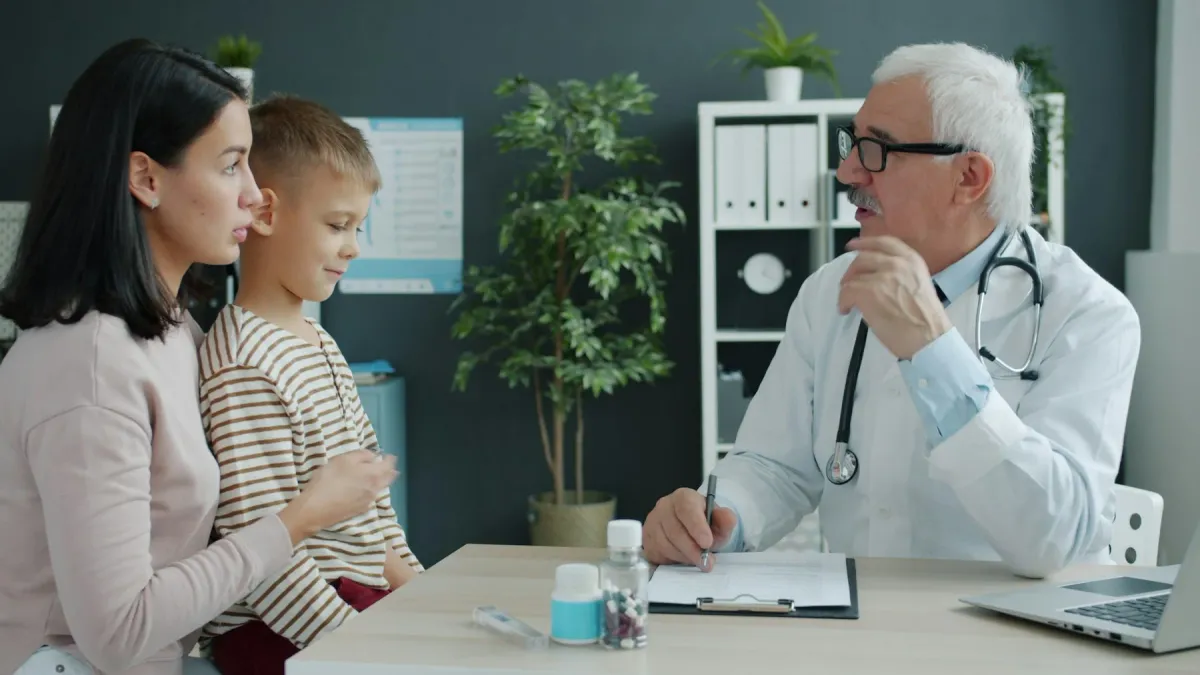 Médico conversa com a mãe e a criança em uma mesa de consultório