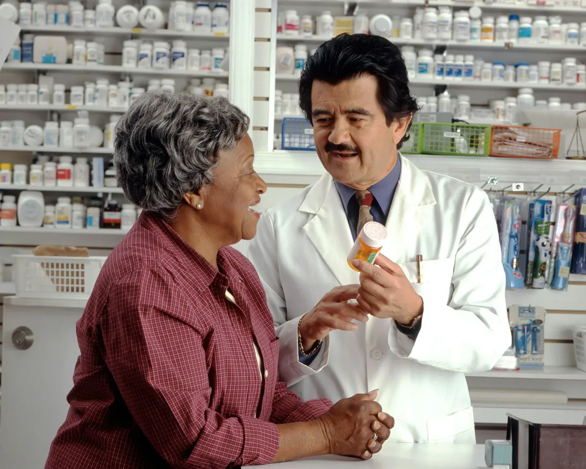 Farmacêutico mostra um frasco de medicamento a uma paciente na farmácia