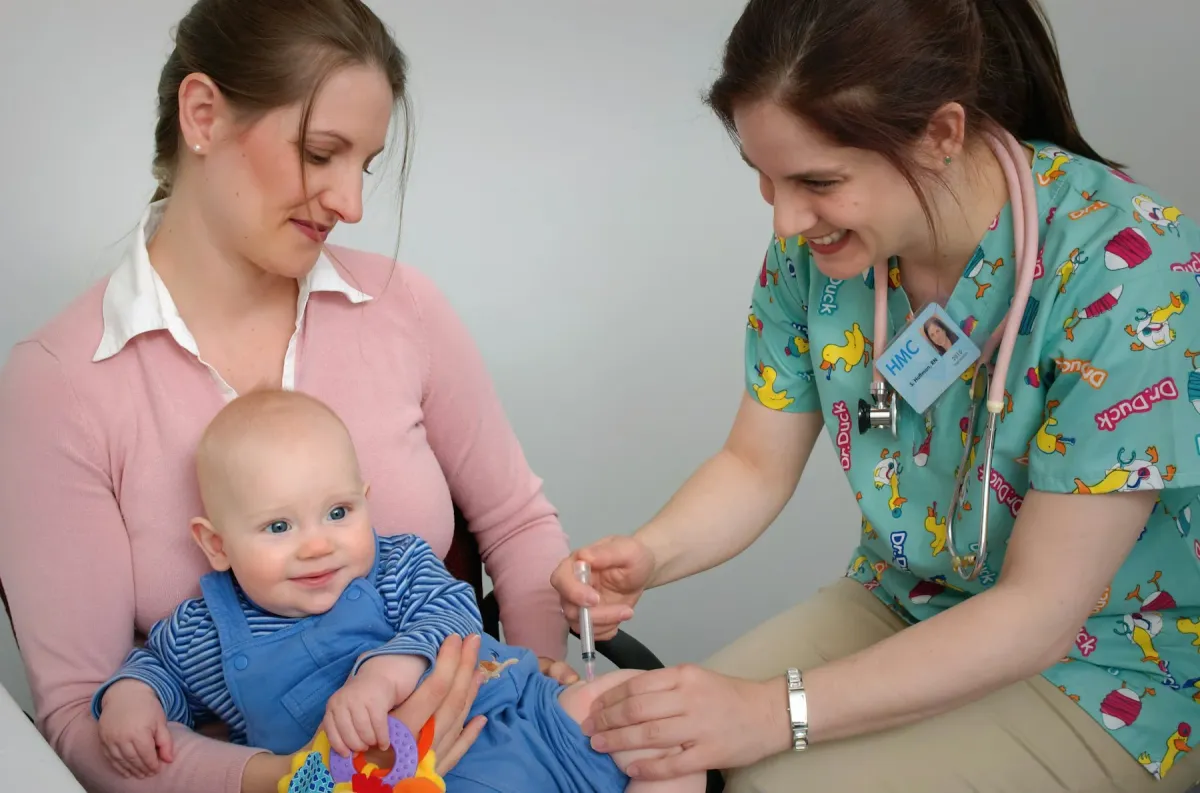 Profissional de saúde atende um bebê sorridente no colo da mãe