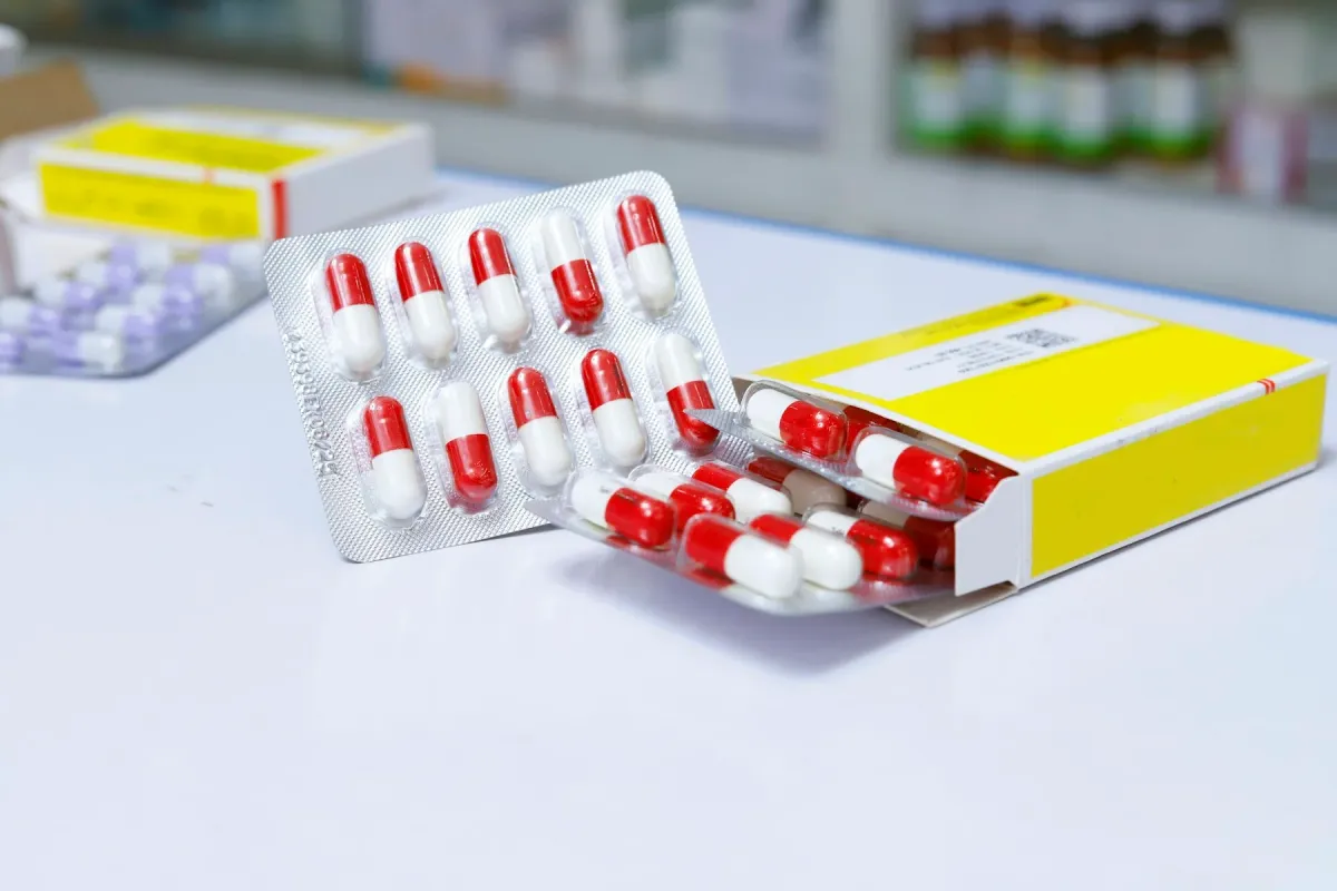 Cartela de cápsulas vermelhas e brancas e caixa de medicamento sobre balcão de farmácia