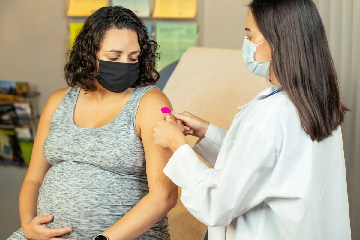 Médica de máscara aplica curativo no braço de uma gestante de máscara após vacina