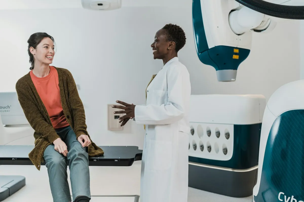 Médica de jaleco conversa com paciente em sala de exames