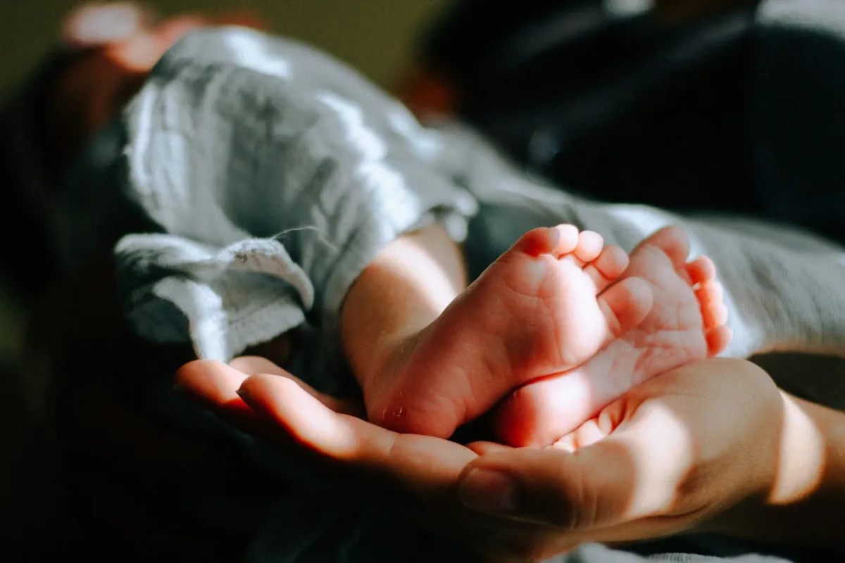 Mãos seguram com cuidado os pezinhos de um recém-nascido