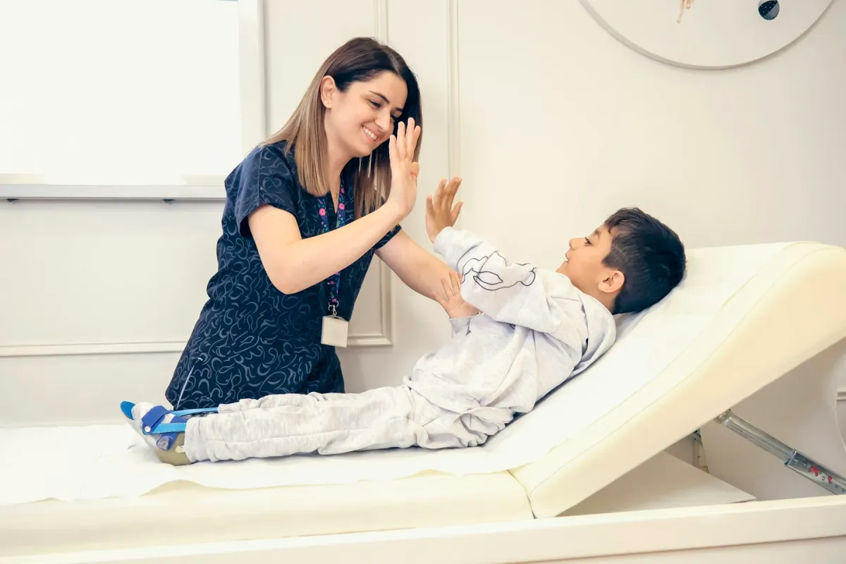 Profissional de saúde cumprimenta um menino deitado na maca com um high five