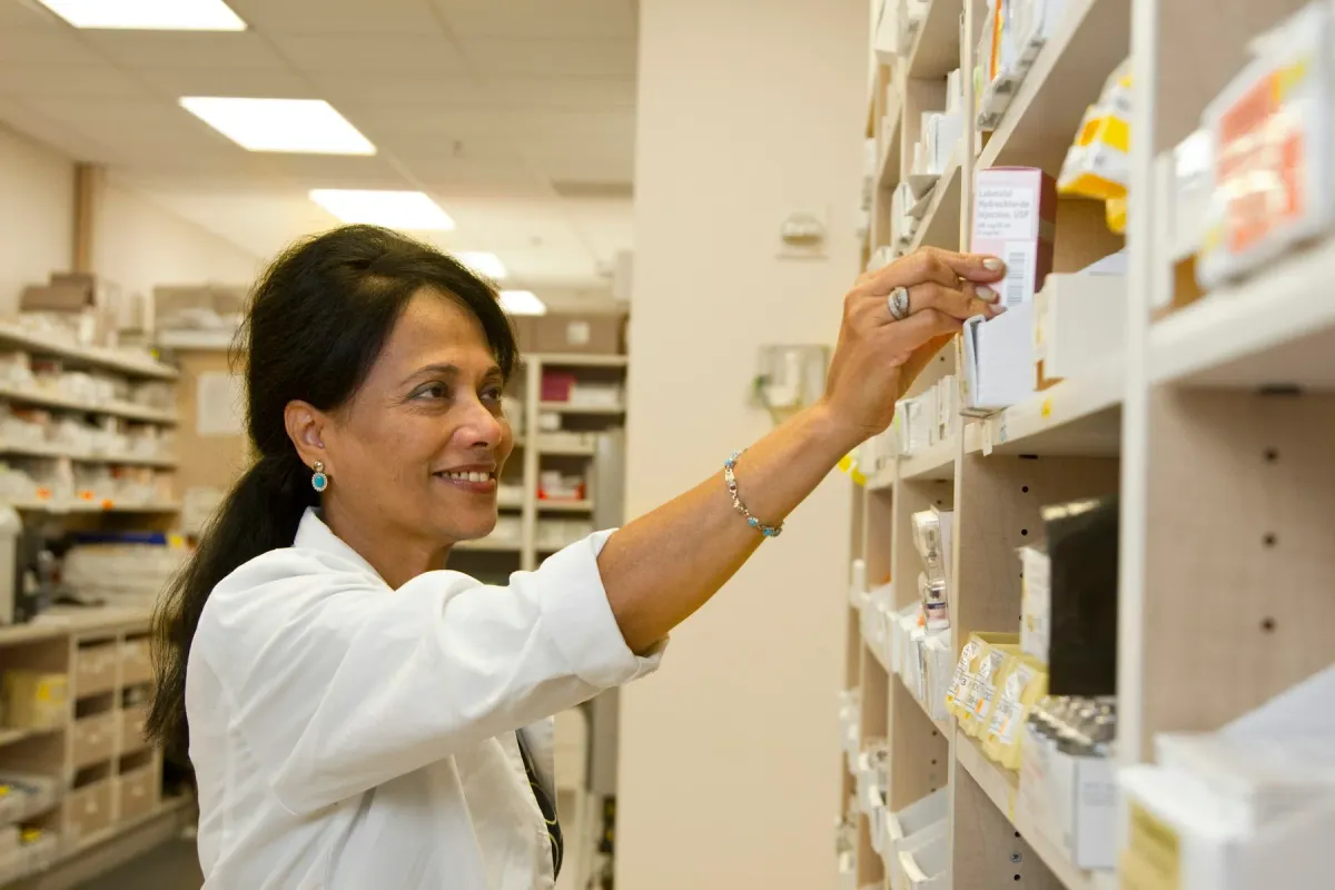 Farmacêutica sorridente alcança uma caixa de medicamento na prateleira