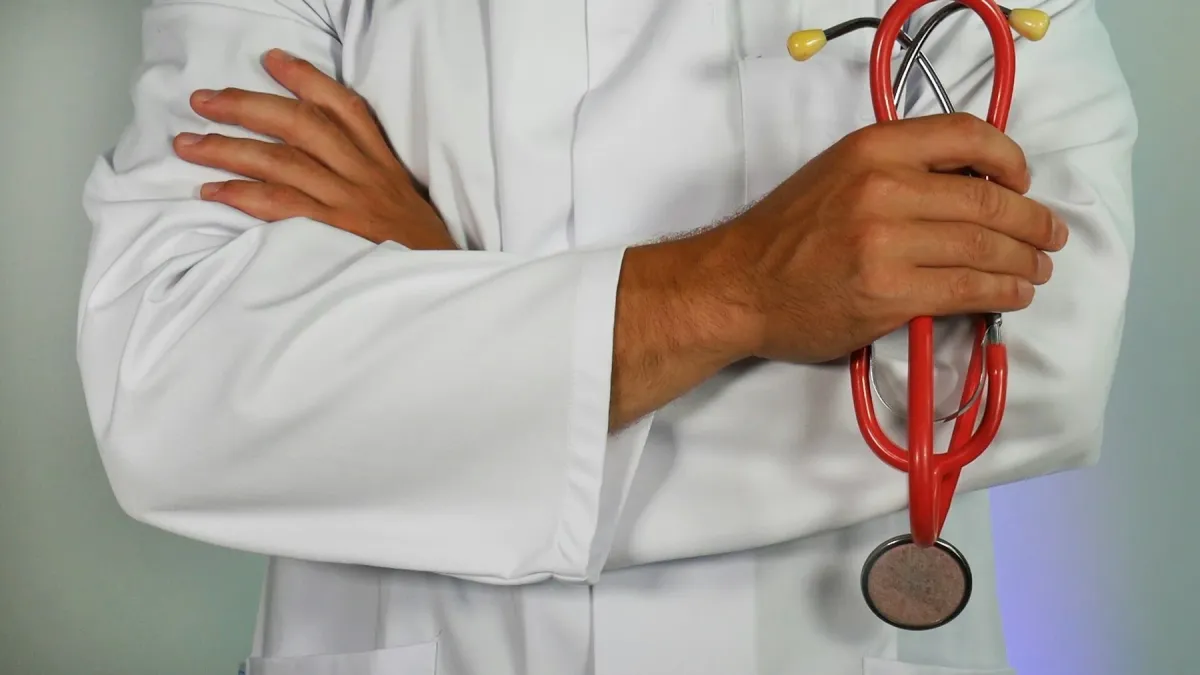 Médico de jaleco branco segurando um estetoscópio vermelho