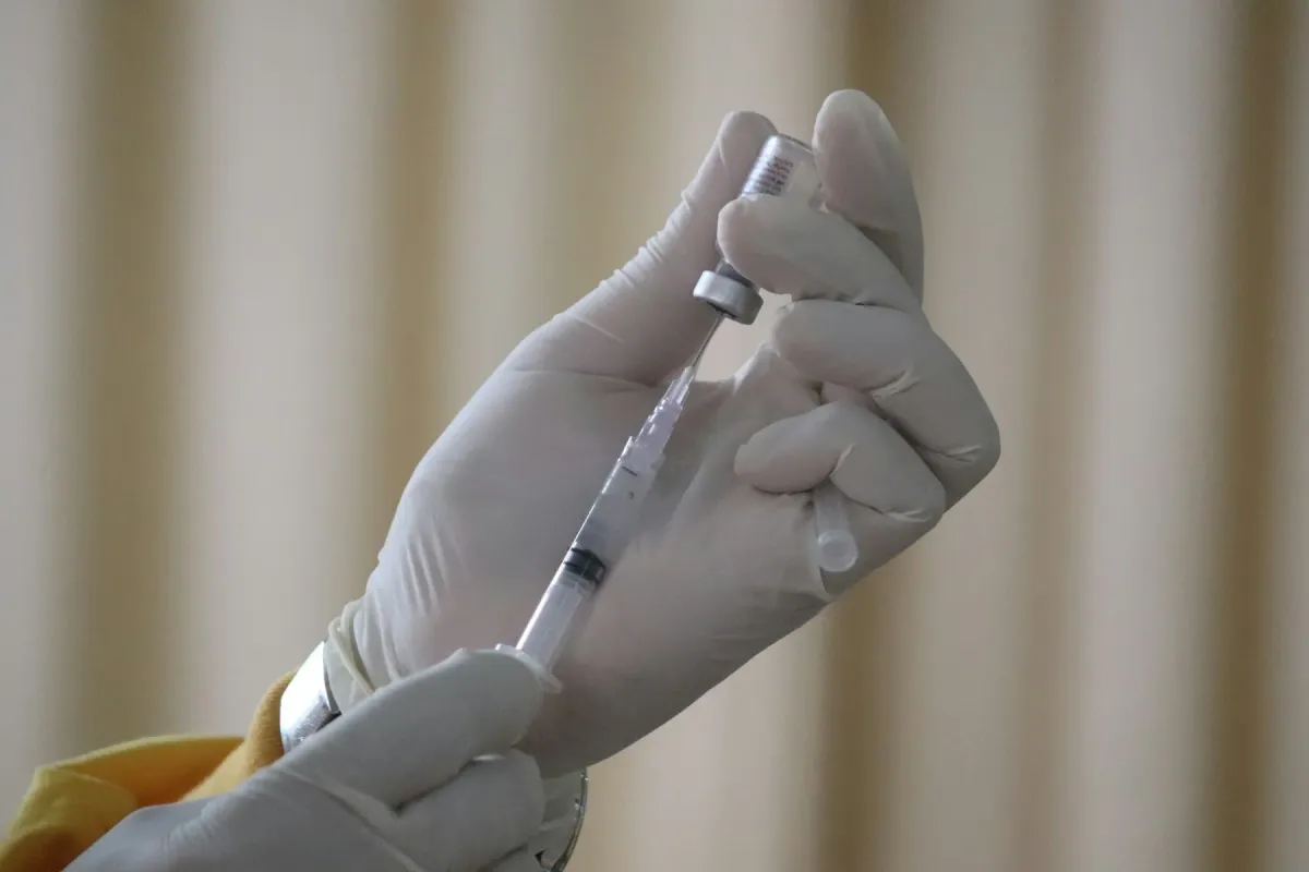 Mãos enluvadas aspirando medicamento de um frasco com seringa