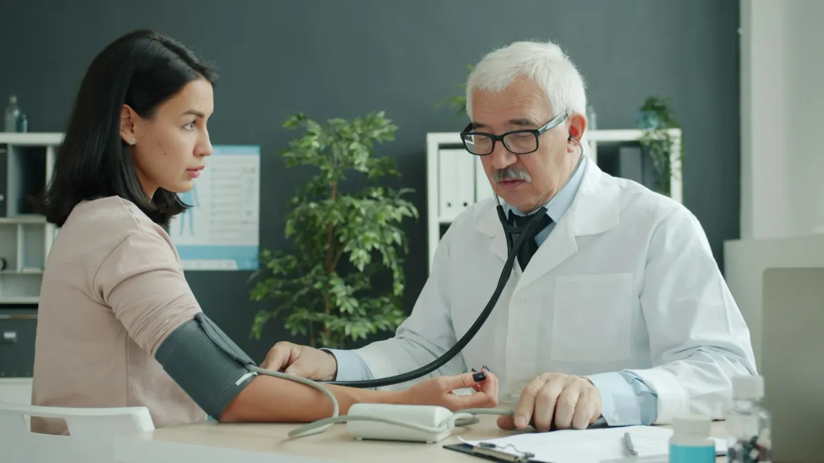 Médico idoso mede a pressão de uma paciente jovem com estetoscópio