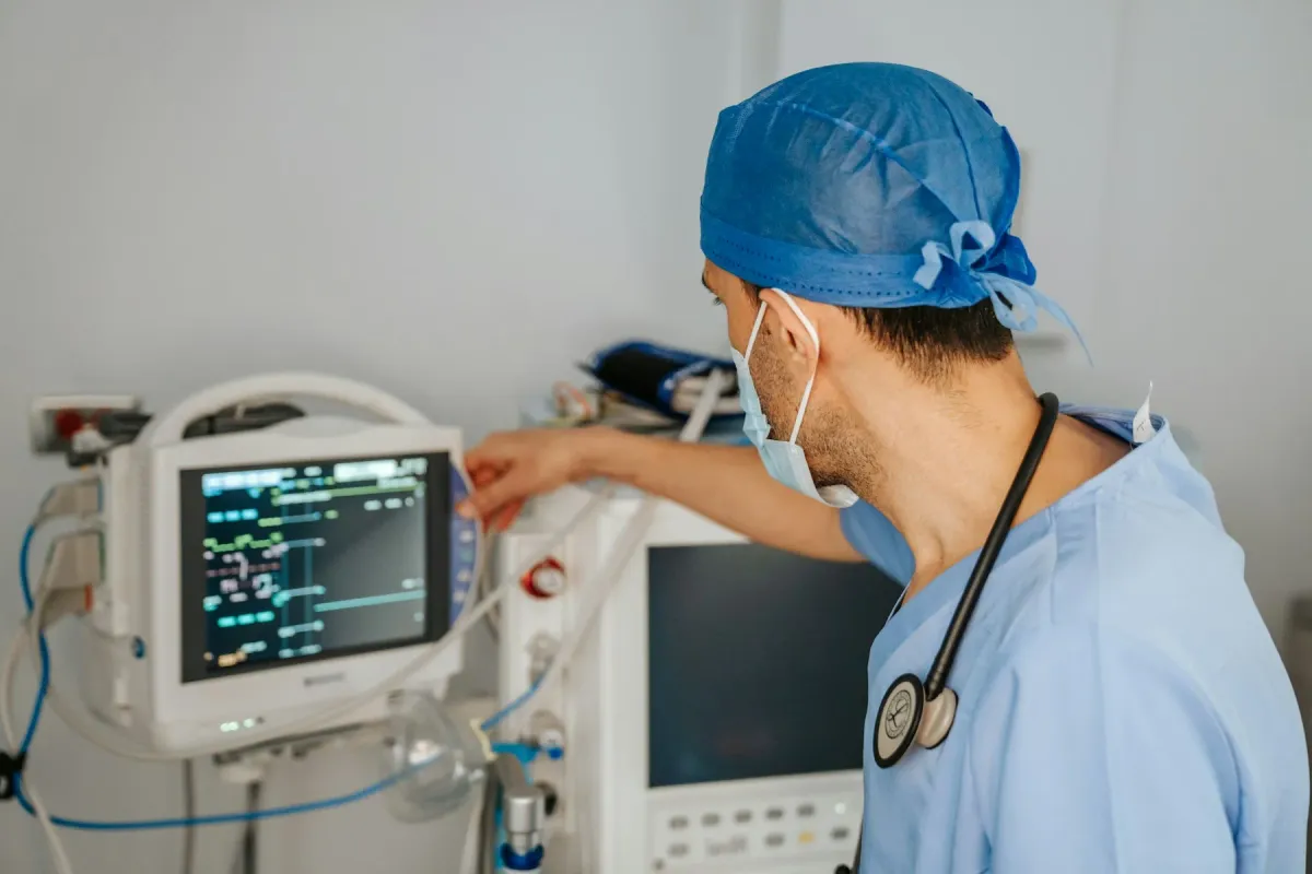 Intensivista de uniforme azul ajusta o monitor ao lado do ventilador na UTI