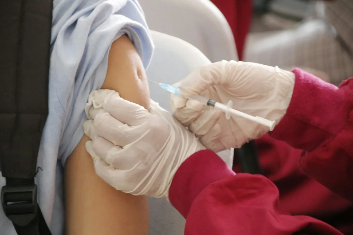 Profissional de luvas aplica injeção no braço de uma pessoa