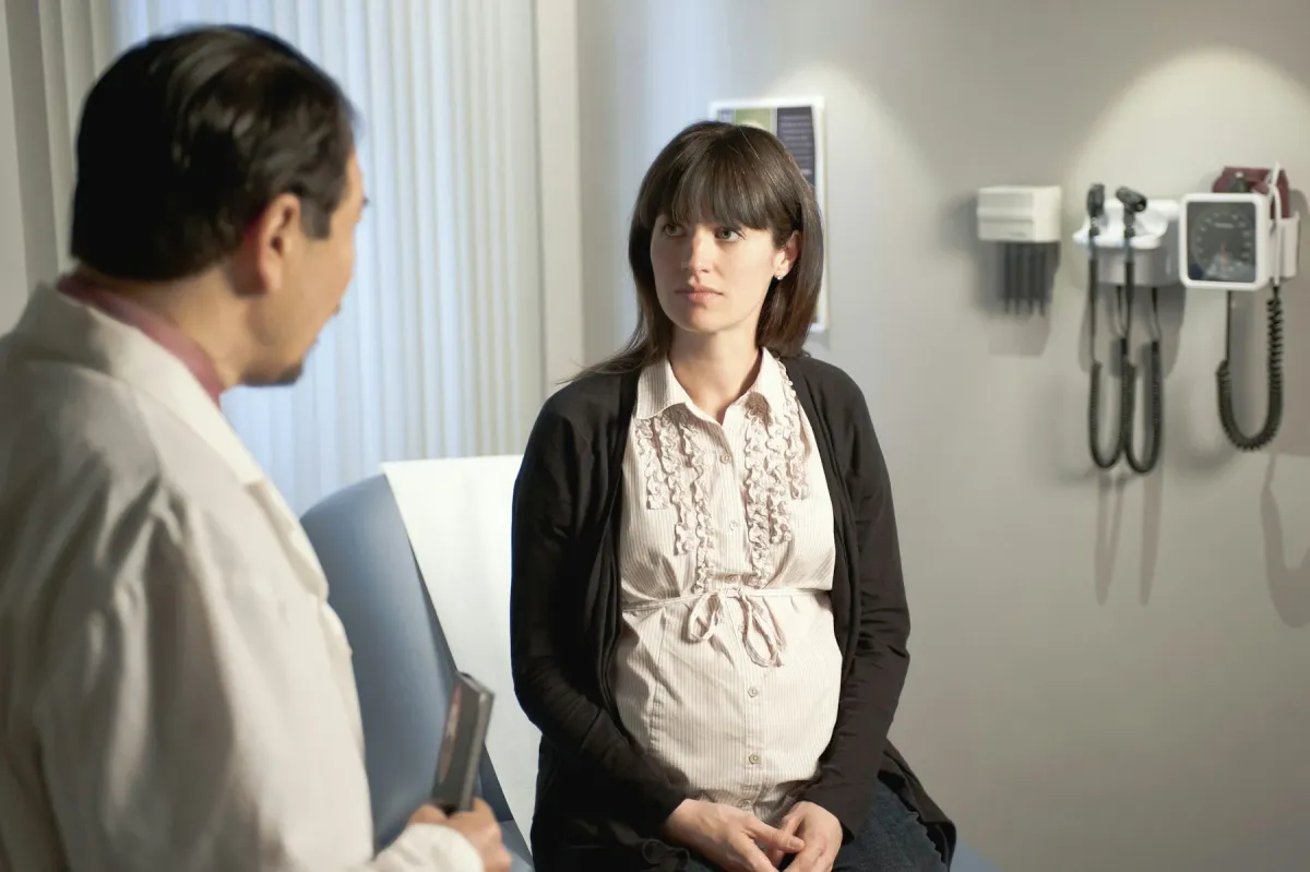 Médico conversa com uma gestante sentada no consultório