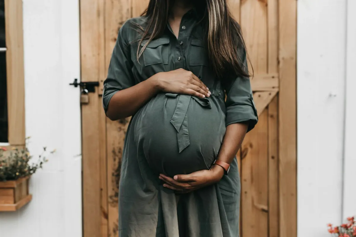 Gestante de vestido verde segura a barriga diante de uma porta de madeira