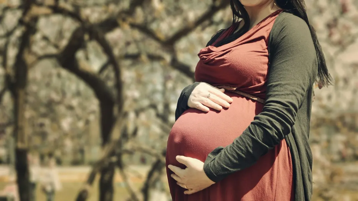 Gestante de vestido vermelho apoia as mãos na barriga ao ar livre