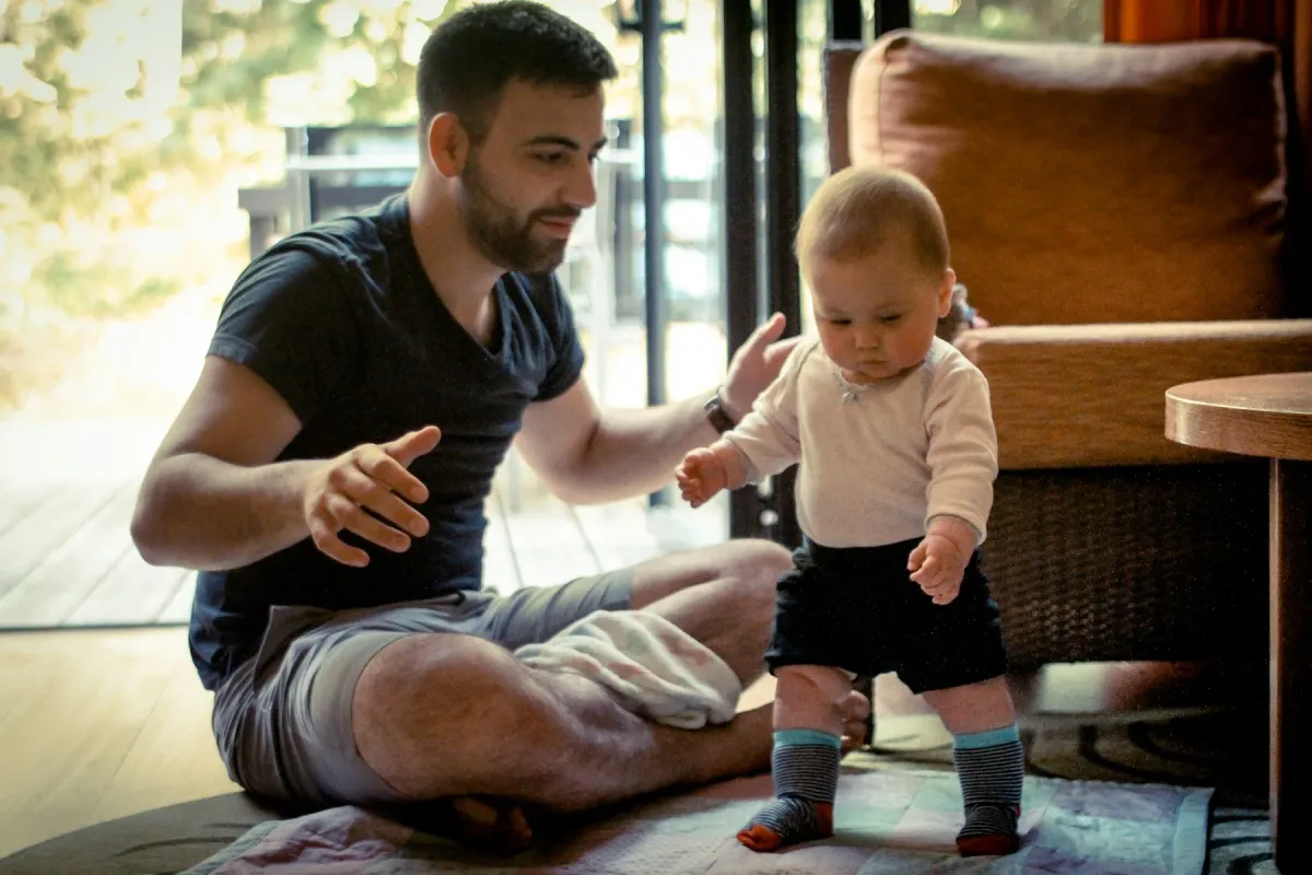 Pai ajuda o bebê a dar os primeiros passos dentro de casa