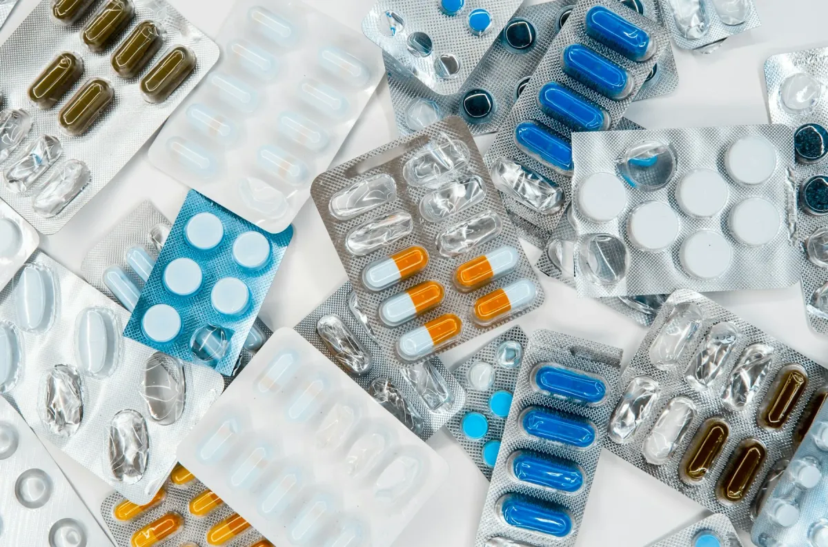 Várias cartelas de comprimidos e cápsulas de cores diferentes sobre uma mesa