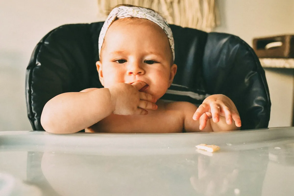 Bebê sentado na cadeirinha com a mão na boca