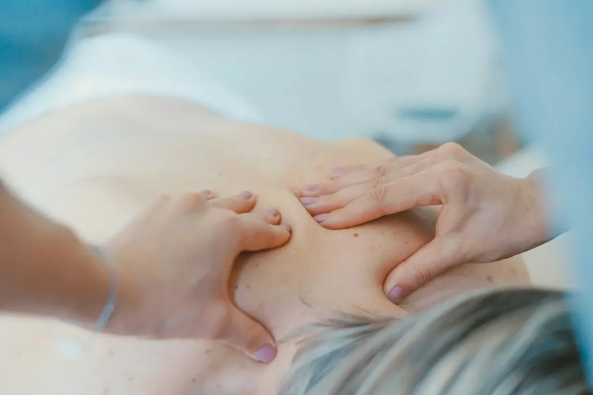 Mãos de fisioterapeuta massageiam o ombro e as costas de uma paciente