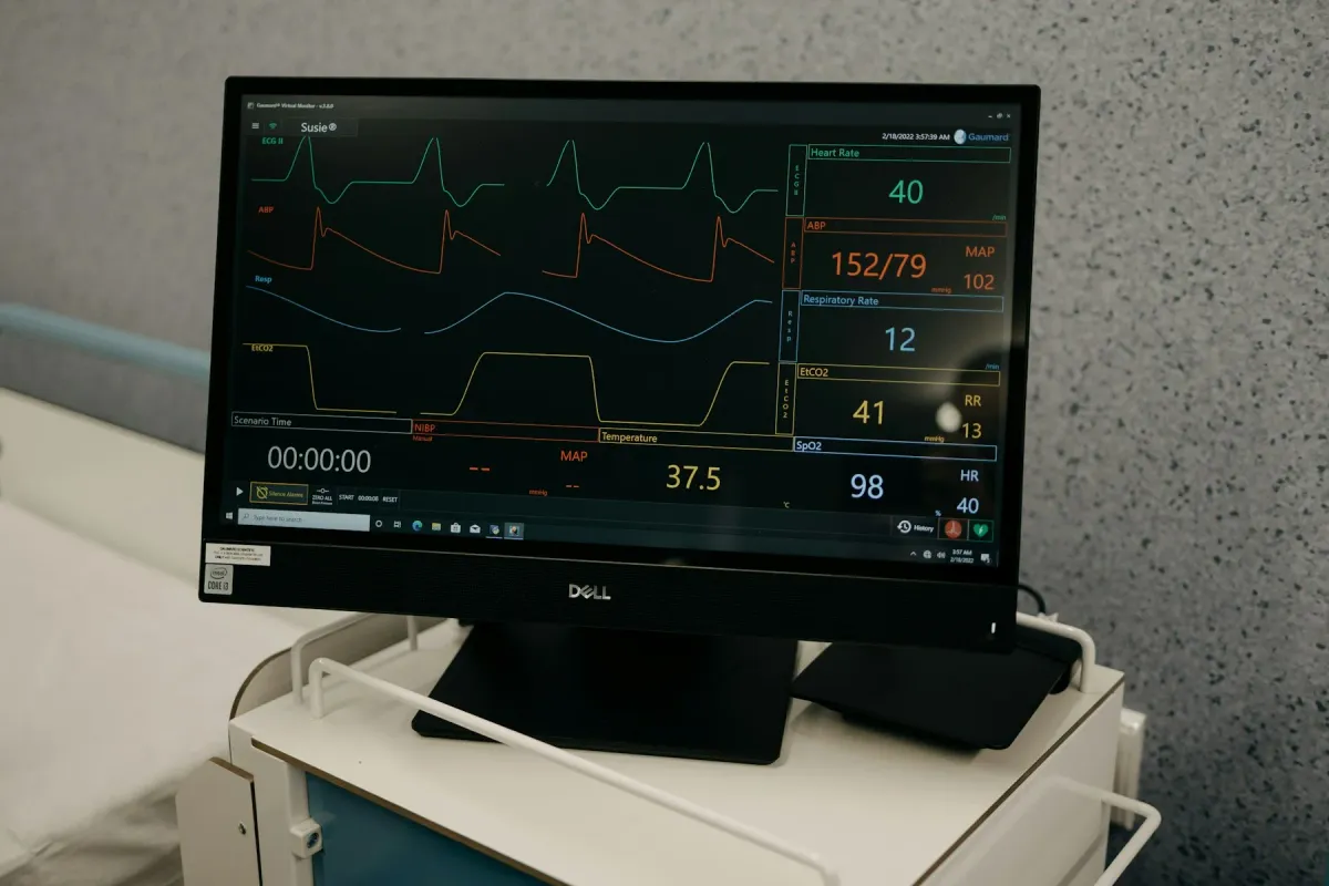 Monitor com traçados de ECG e sinais vitais sobre suporte em ambiente hospitalar