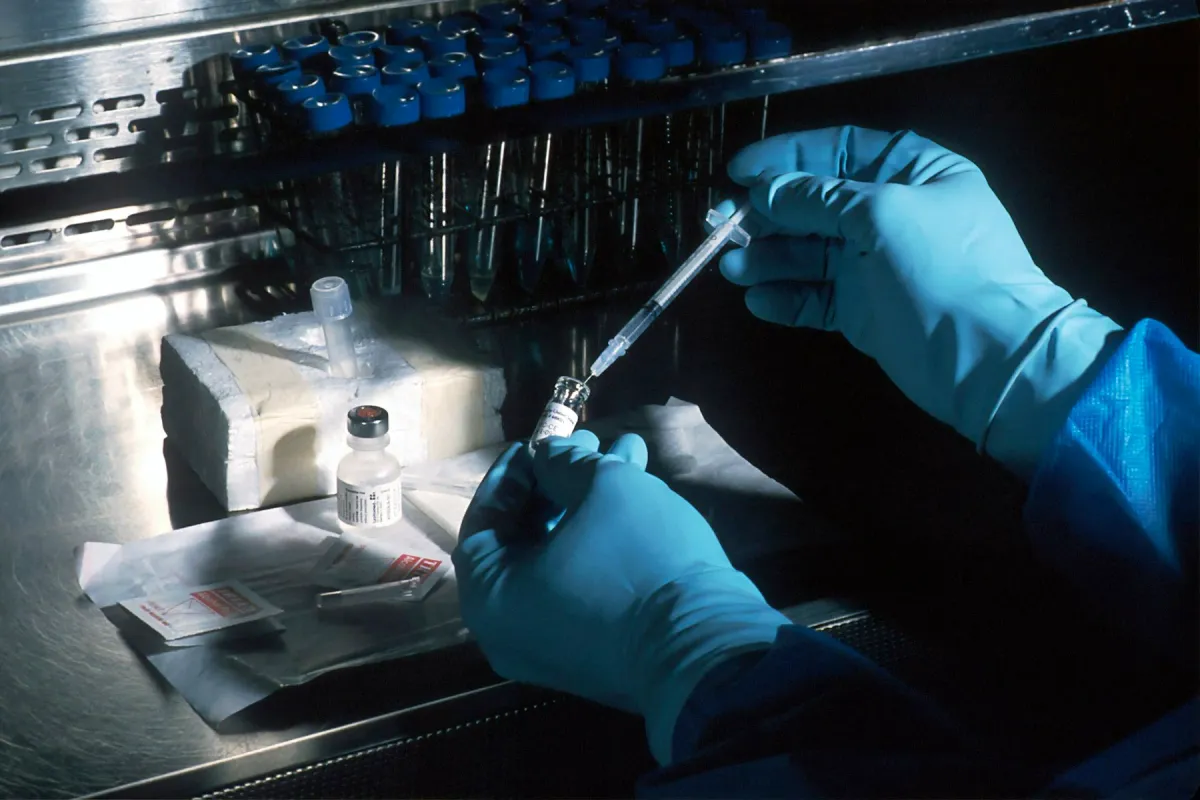 Mãos enluvadas preparam uma seringa a partir de um frasco de medicamento