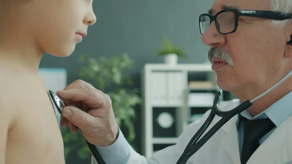 Médico de óculos examina o peito de um menino com estetoscópio