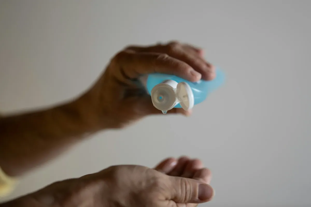 Mãos segurando um tubo de gel ou creme, deixando cair uma gota