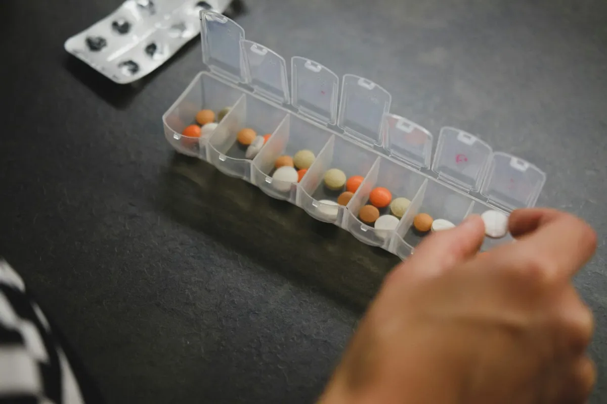 Mão separando comprimidos coloridos em um organizador semanal de medicamentos