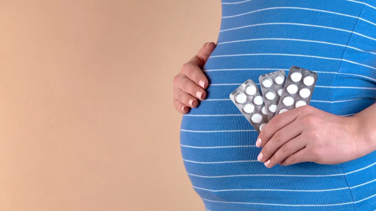 Gestante de vestido azul listrado segura cartelas de comprimidos junto à barriga