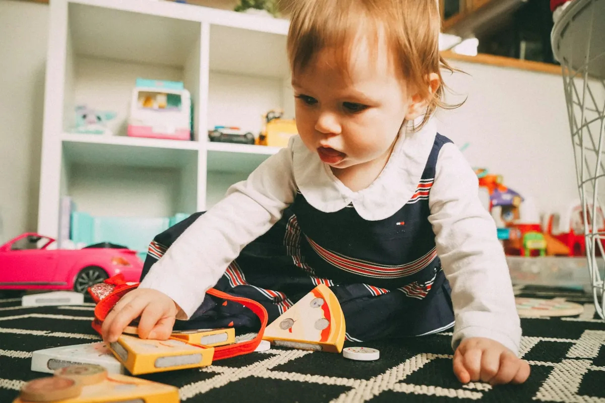 Criança pequena brincando no chão de um quarto com brinquedos