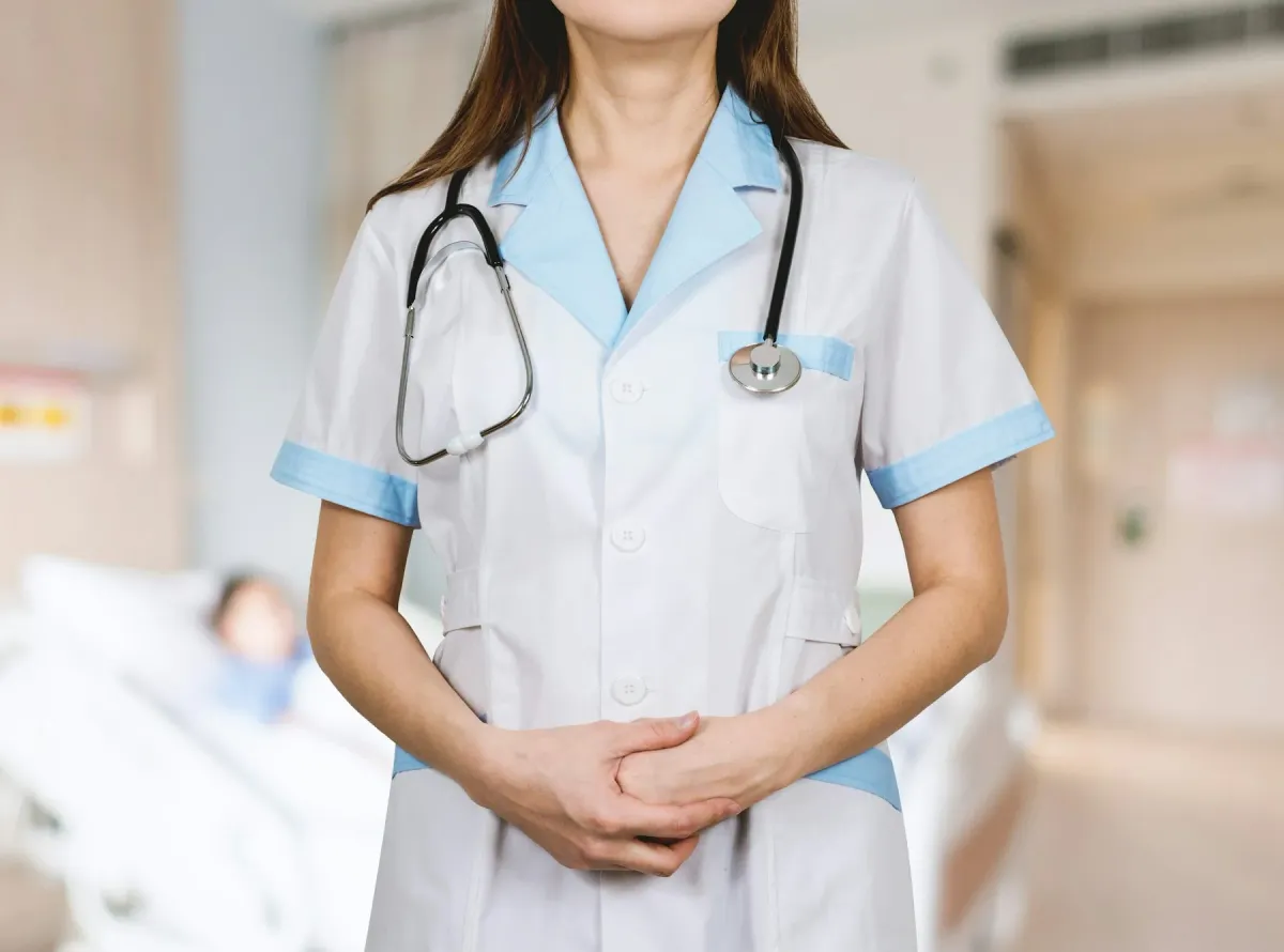 Profissional de saúde de uniforme branco e azul com estetoscópio no pescoço em corredor hospitalar