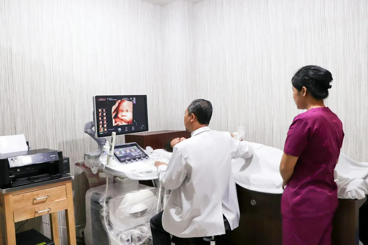 Médico realiza ultrassonografia em gestante deitada, com auxiliar ao lado do equipamento