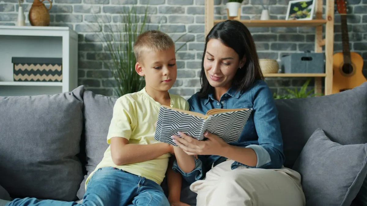 Mãe e filho sentados no sofá folheando um livro juntos