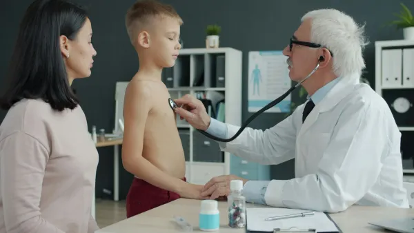 Médico ausculta o tórax de um menino com estetoscópio enquanto a mãe observa
