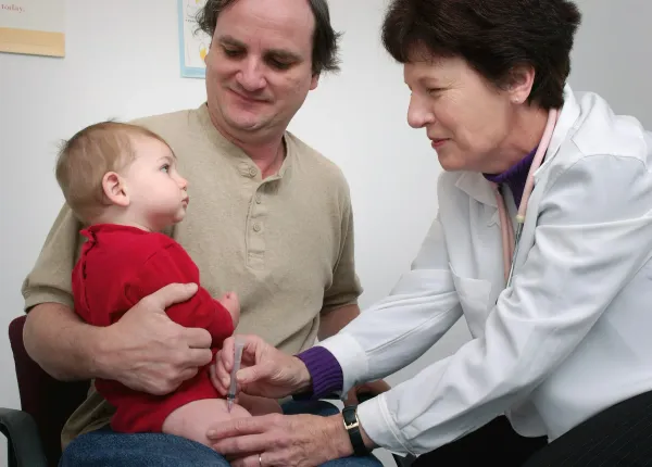 Médica examina um bebê no colo do pai durante a consulta