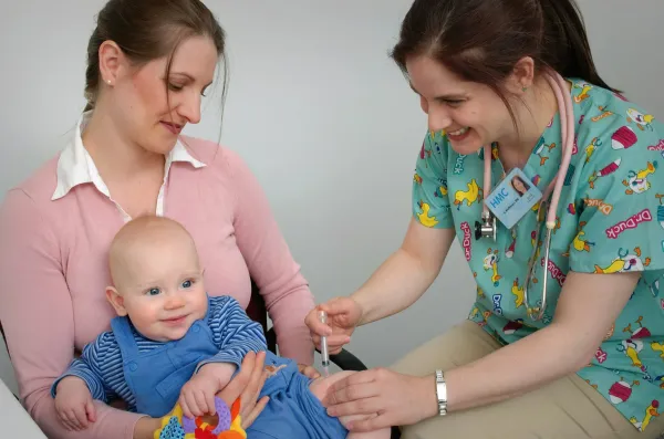Profissional de saúde atende um bebê sorridente no colo da mãe