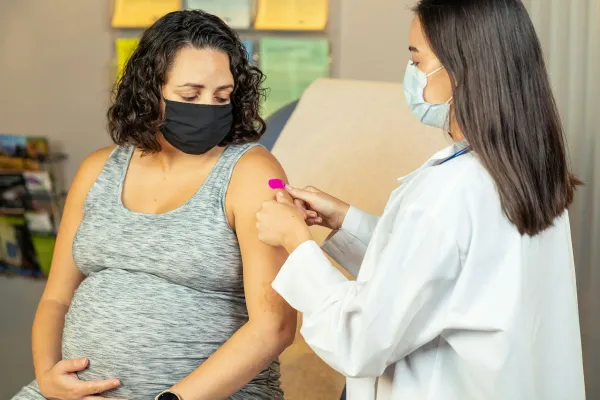 Médica de máscara aplica curativo no braço de uma gestante de máscara após vacina
