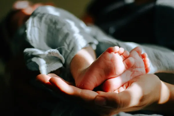 Mãos seguram com cuidado os pezinhos de um recém-nascido