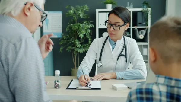 Médica anota na consulta enquanto o avô e o neto aguardam