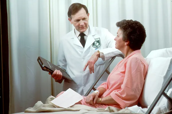 Médico de jaleco conversa com paciente sentada no leito hospitalar
