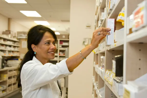 Farmacêutica sorridente alcança uma caixa de medicamento na prateleira