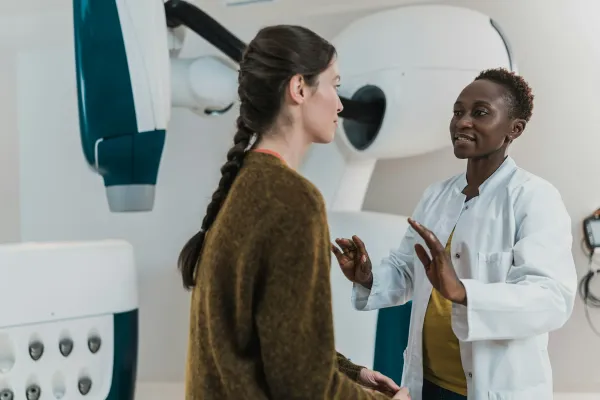 Médica de jaleco conversa com paciente ao lado de equipamento hospitalar