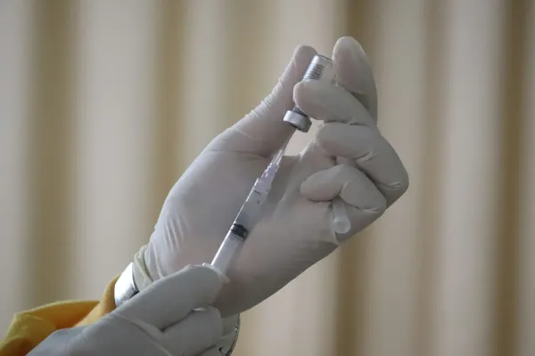 Mãos enluvadas aspirando medicamento de um frasco com seringa
