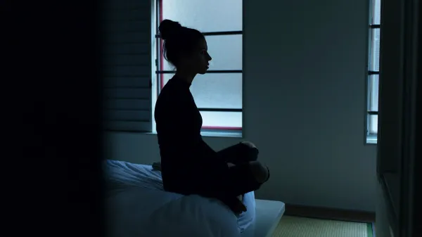 Silhueta de mulher sentada sobre a cama em quarto escuro