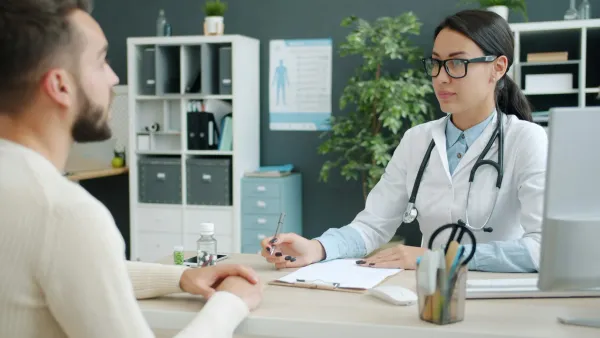 Médica conversa com um paciente em consultório enquanto anota na prancheta