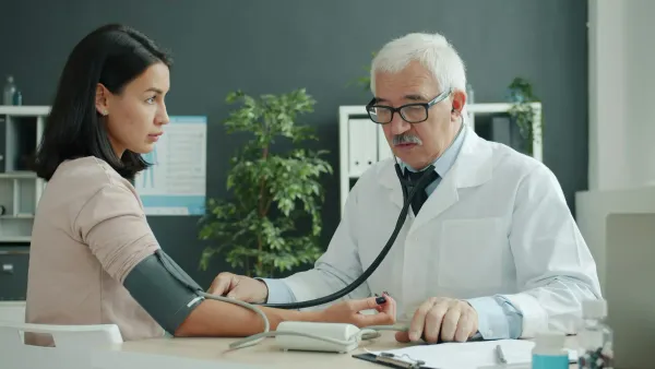 Médico idoso mede a pressão de uma paciente jovem com estetoscópio