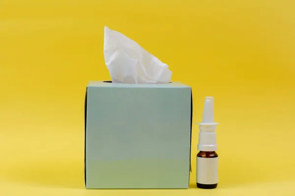 Caixa de lenços de papel ao lado de um frasco de spray nasal